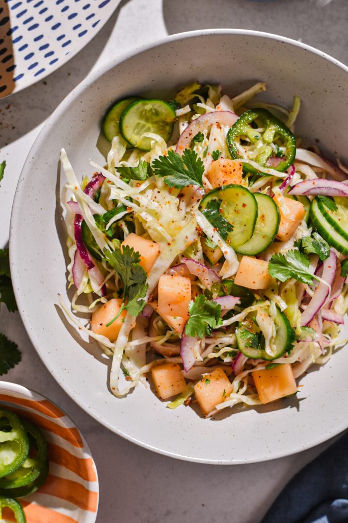 Overhead shot of cabbage cantaloupe slaw in a white bowl, garnished with some tajin.
