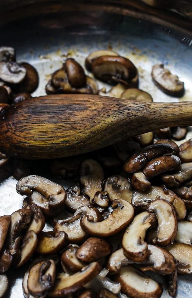 Mushrooms cooking in a skillet with a spoon.