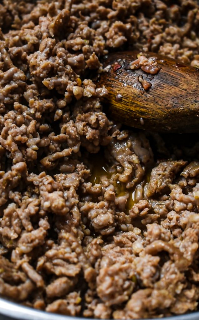 Italian sausage being cooked in a skillet with a wooden spoon.