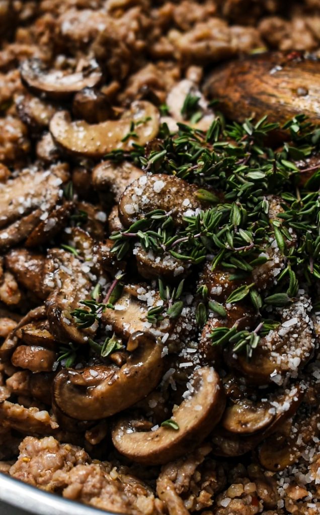 Mushrooms and thyme added to the Italian sausage in a skillet.