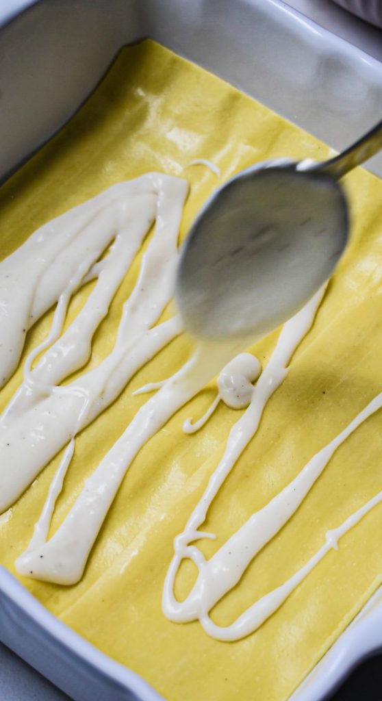 Lasagna noodles in a baking dish being covered in bechamel sauce.