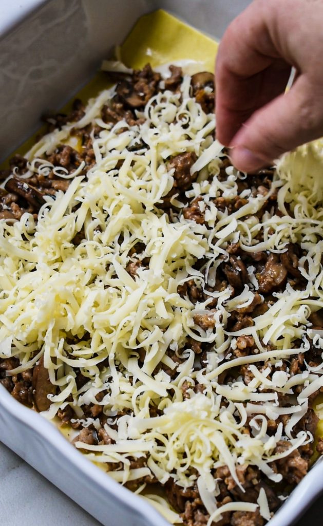 Hand sprinkling the cheese layer on the lasagna.