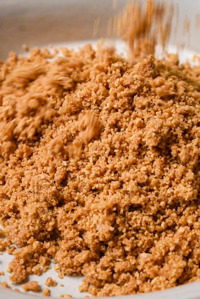 Crushed graham cracker mixture being poured into a pie dis.