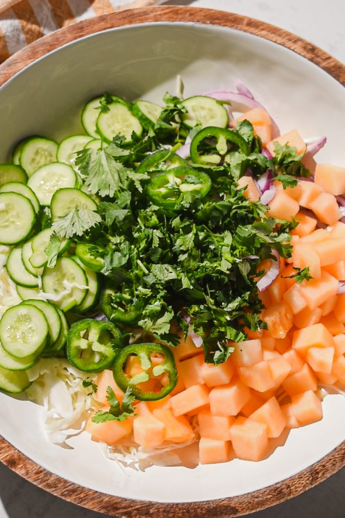Ingredients for cantaloupe cabbage slaw in a bowl.