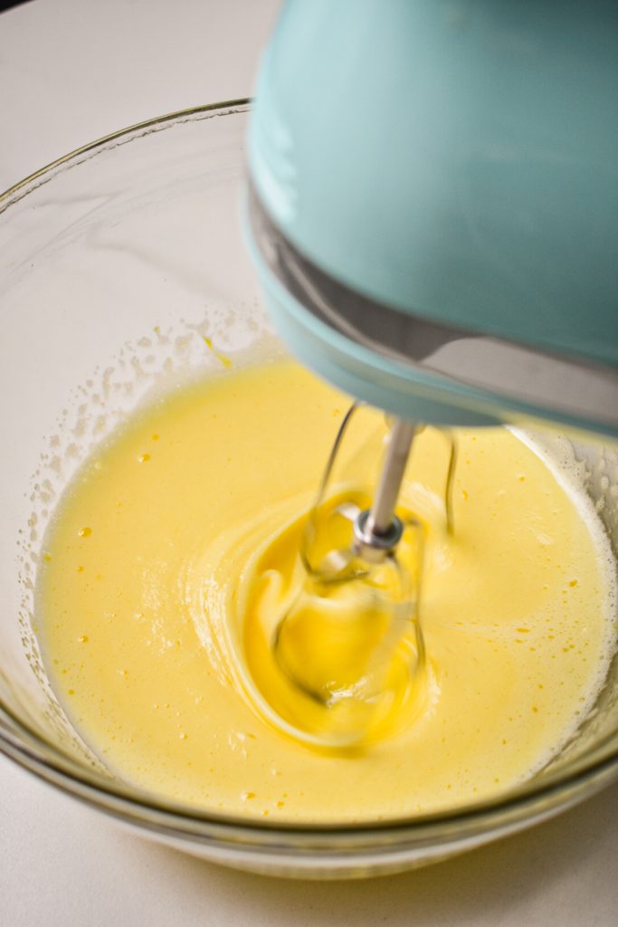 Using a hand mixer to whip up the eggs and sugar.