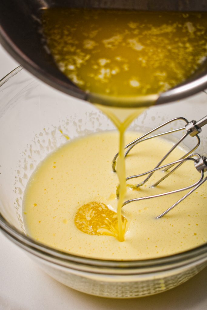 Pouring melted butter into the egg and sugar mixture in the mixing bowl.