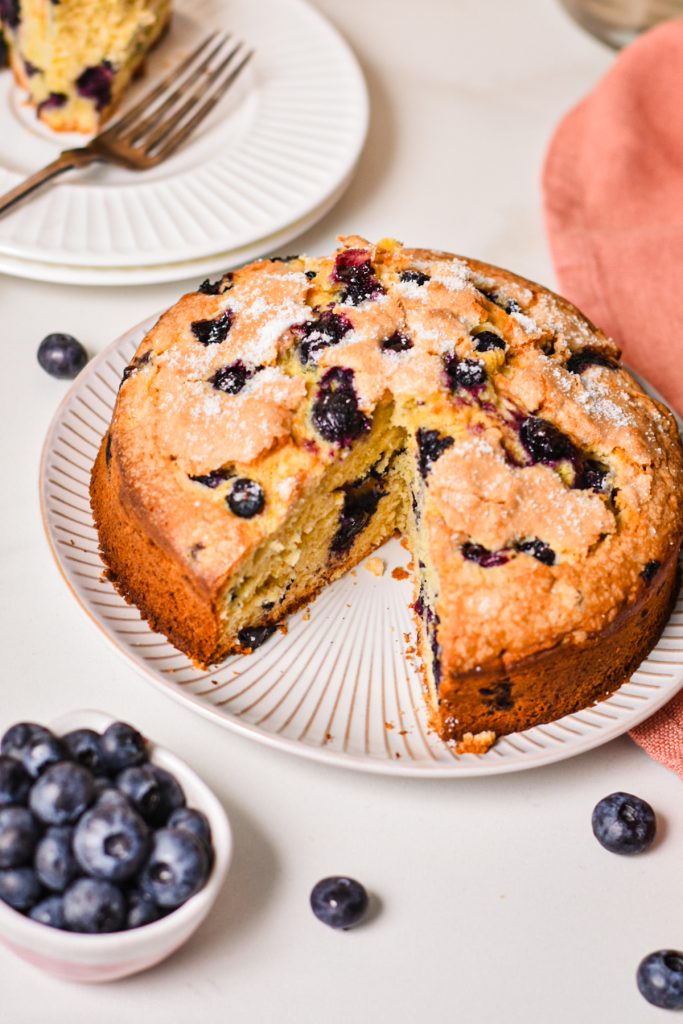 Lemon blueberry torte on a plate with a slice missing and fresh blueberries scattered around.