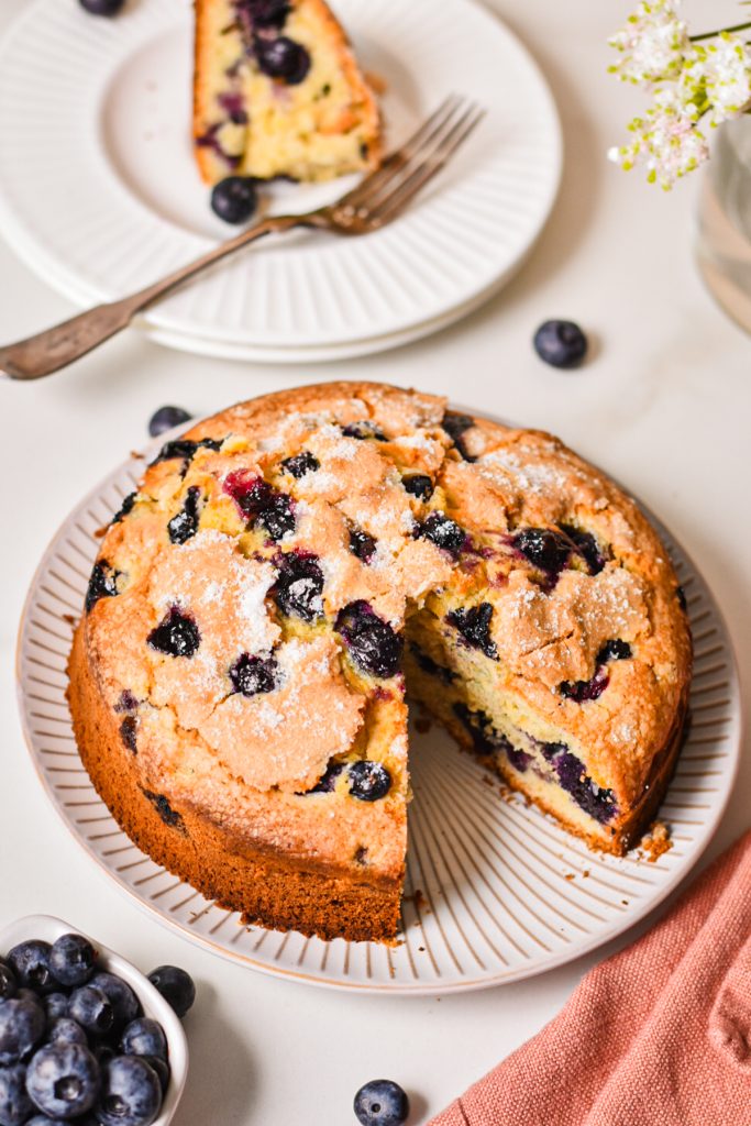 Lemon blueberry torte on a serving plate with a slice of it on a separate plate next to it.