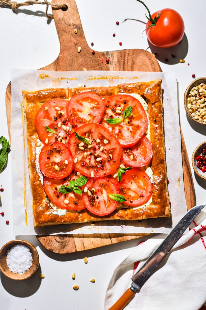 Tomato tart with whipped feta on a wooden cutting board before being sliced.