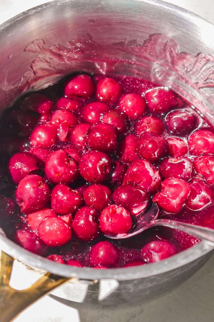 Cherry compote in a saucepan with a spoon.