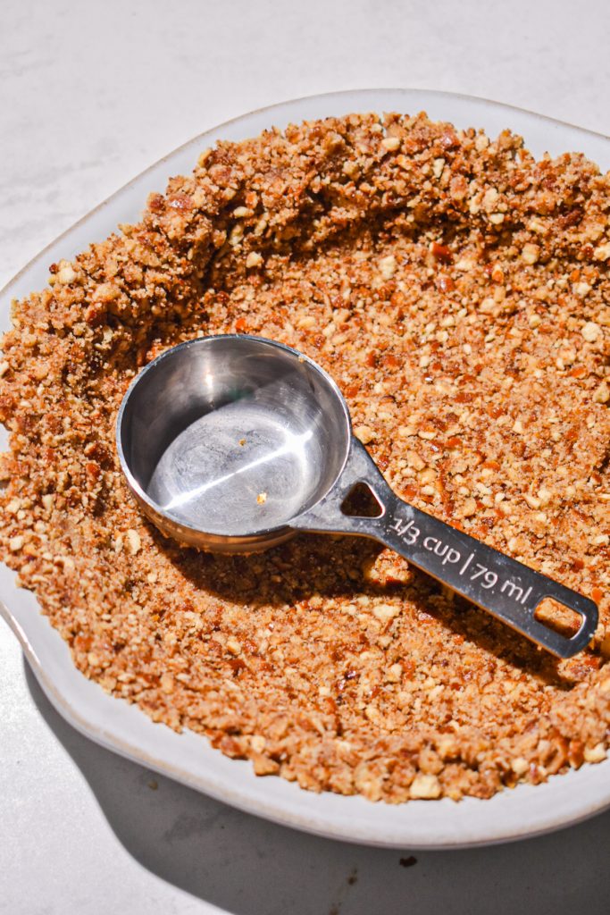 Pressing the crushed pretzels into a pie dish.