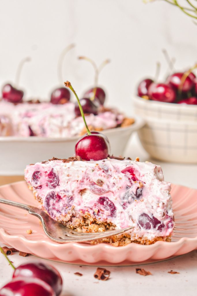 Slice of cherry pretzel pie on a pink plate with a fresh cherry on top.