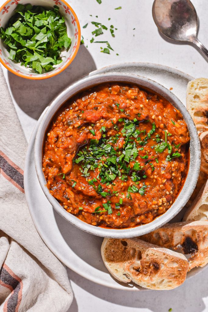 Moroccan eggplant dip served in a bowl with fresh parsley on top and toasted bread on the side.