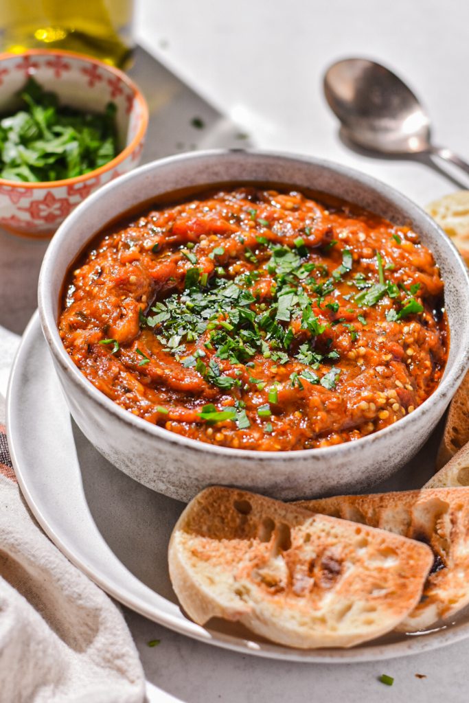 Zaalouk eggplant dip in a small bowl on a plate with toasted pieces of bread.