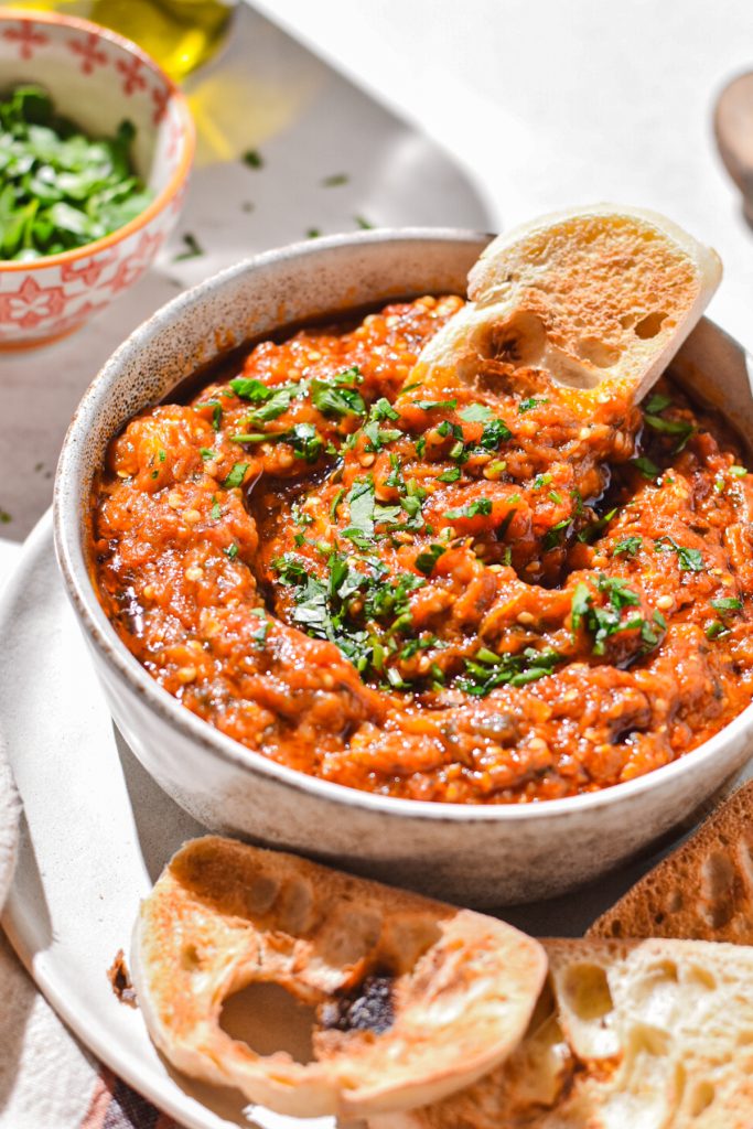 Piece of toasted bread being dipped into the eggplant dip.