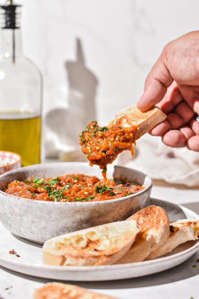 Hand holding a piece of toasted bread after it was dipped into the zaalouk.