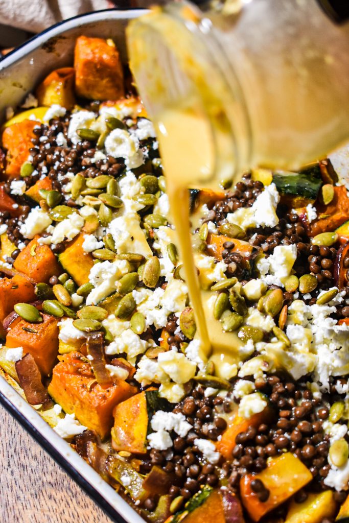 Dressing being poured from a jar into the squash and lentil salad.