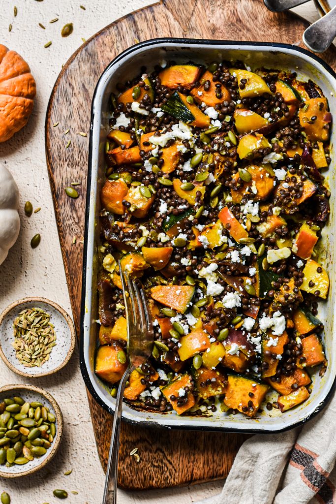 Roasted squash and lentil salad served in a baking dish next to extra toppings on the side.