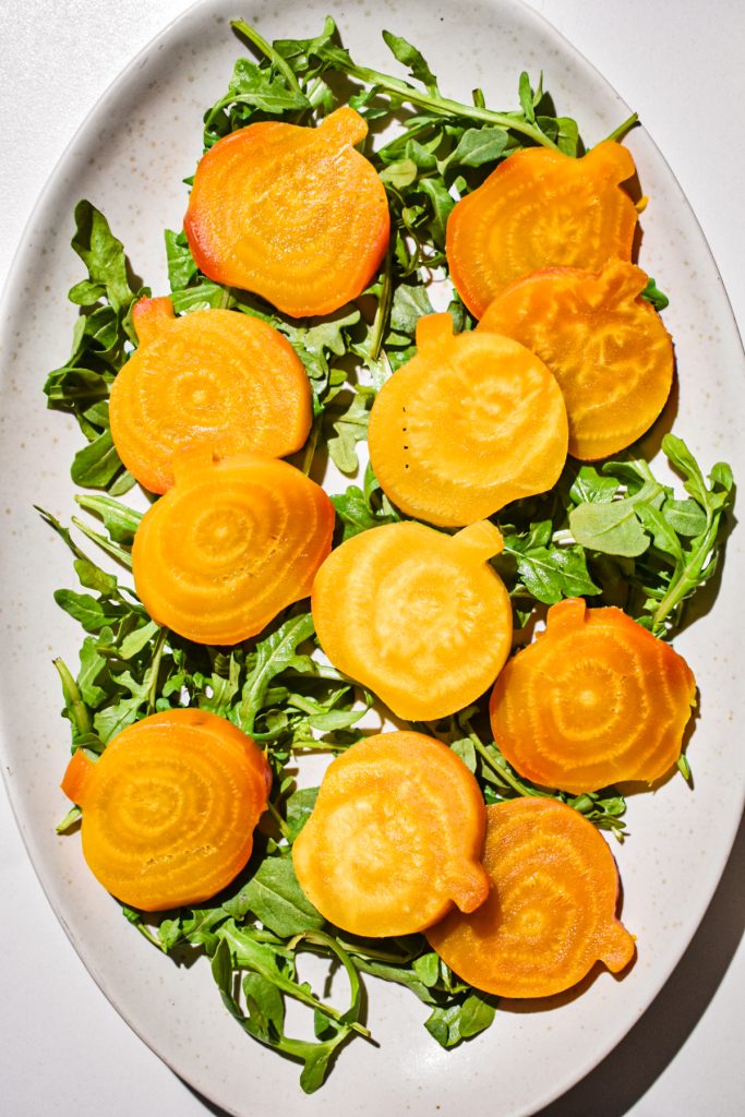 Arugula on a platter topped with pumpkin shaped golden beets.