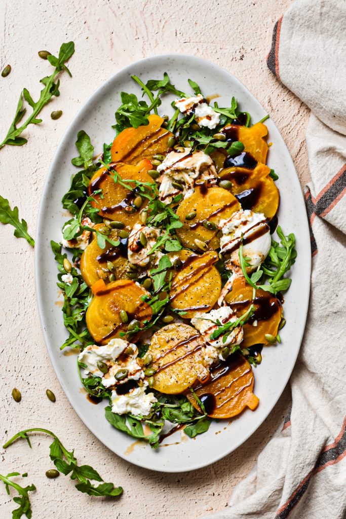 Golden beets and burrata salad served on a white platter with a drizzle of balsamic on top.