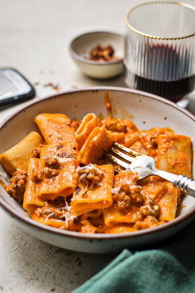 Bowl of red pepper pasta with Italian sausage with a fork in the bowl.