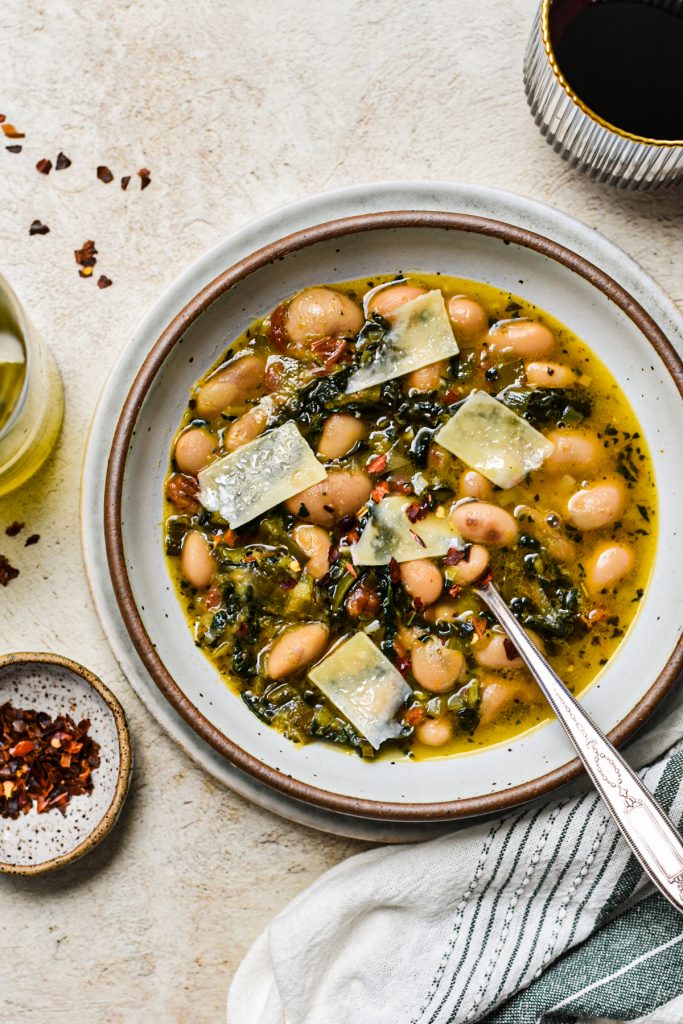 Overhead shot of butter beans and leeks soup with kale in a bowl topped of with shavings of parmesan.