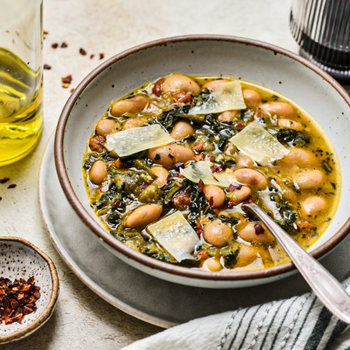 Bowl of butter beans and kale soup with parmesan shavings on top.
