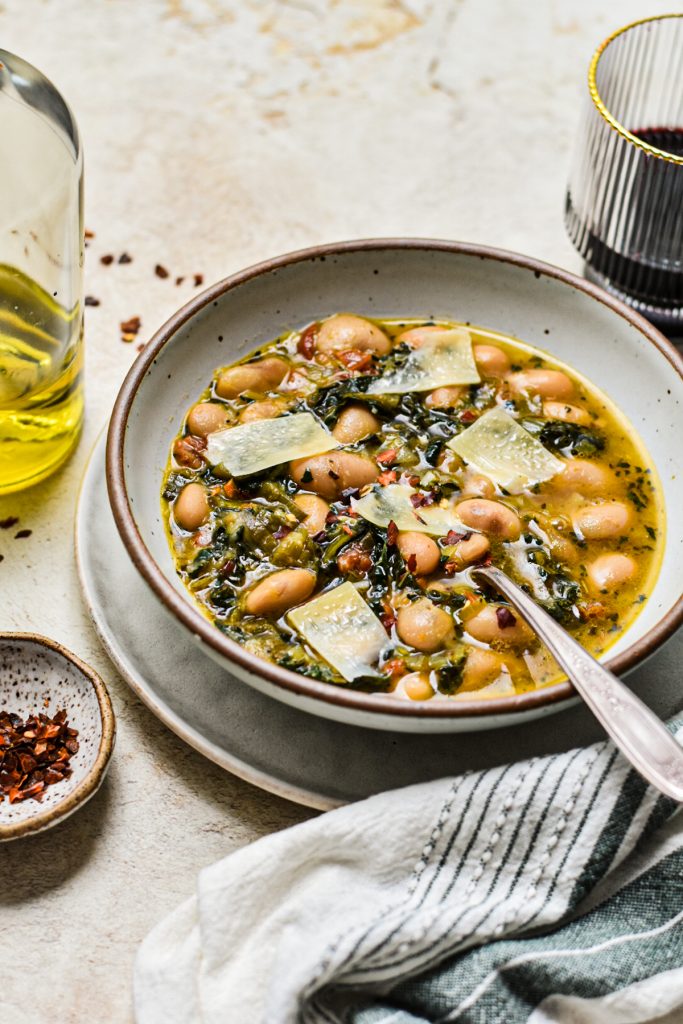 Bowl of butter beans and kale soup with parmesan shavings on top.