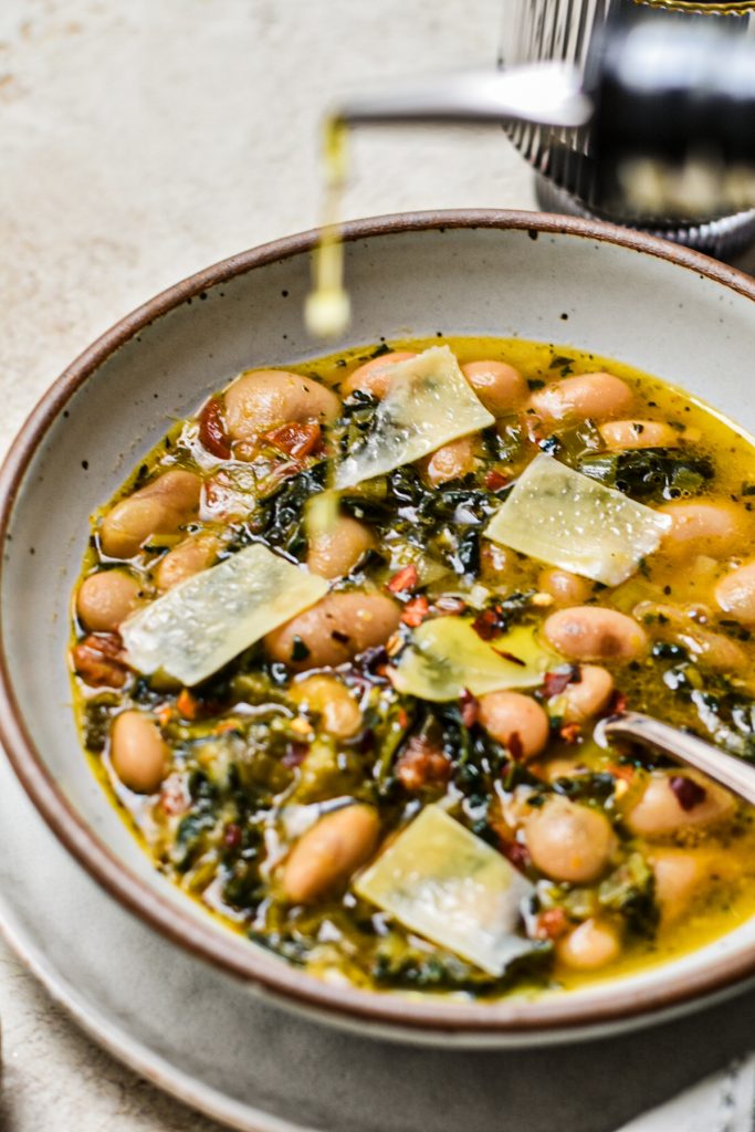 Drizzling olive oil on top of a finished bowl of butter beans with leeks and kale soup.