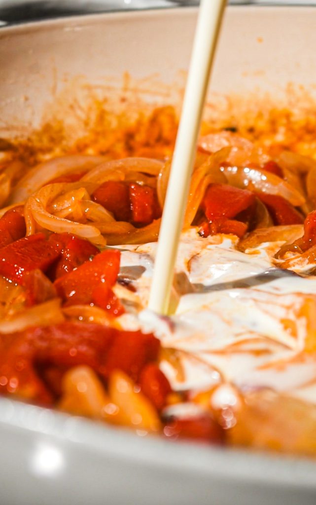 Adding the heavy cream into the onion and pepper mixture in a skillet.