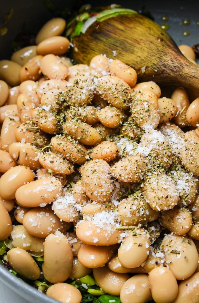 Butter beans in a stock pot being seasoned with salt and pepper.