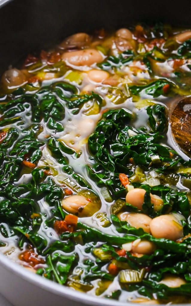 Chopped kale being added to the butter bean soup in a stock pot.
