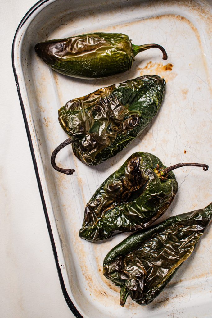 Roasted poblano peppers and one jalapeno pepper in a baking dish.