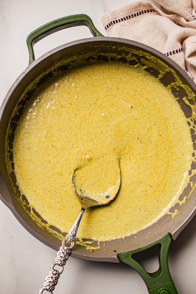 Beer cheese sauce in a skillet with a spoon.