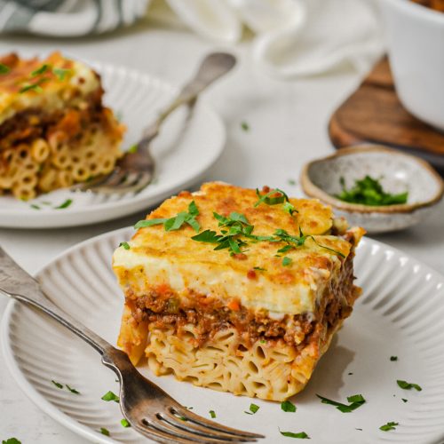 Two plates served with a slice of Greek pastitsio garnished with parsley.