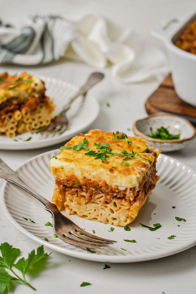 Two plates served with a slice of Greek pastitsio garnished with parsley.