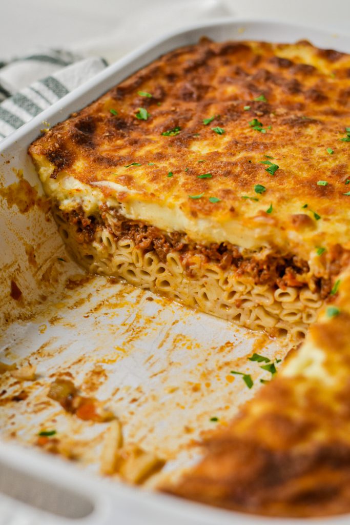 Greek pastitsio baked in a white baking dish with some missing to show the inside layers.