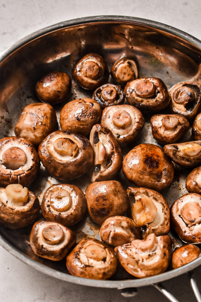 Mushrooms being cooked in a skillet to remove some of their liquid.