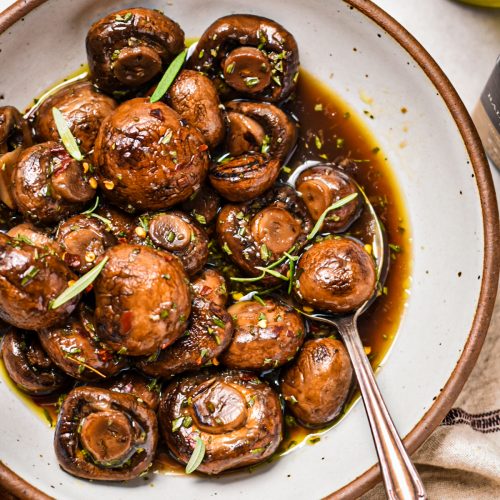 Balsamic marinated mushrooms in a serving bowl with a silver spoon.
