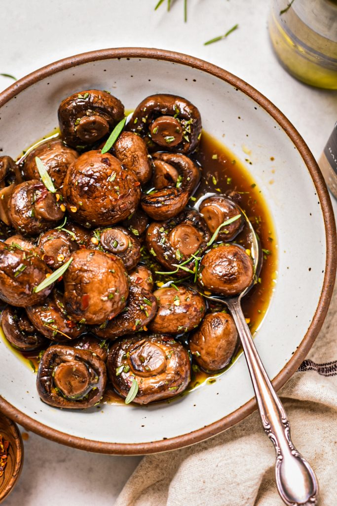 Balsamic marinated mushrooms in a serving bowl with a silver spoon.