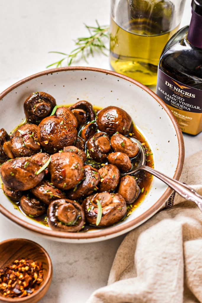 Marinated mushroom salad served in a bowl next to two containers of olive oil and vinegar.