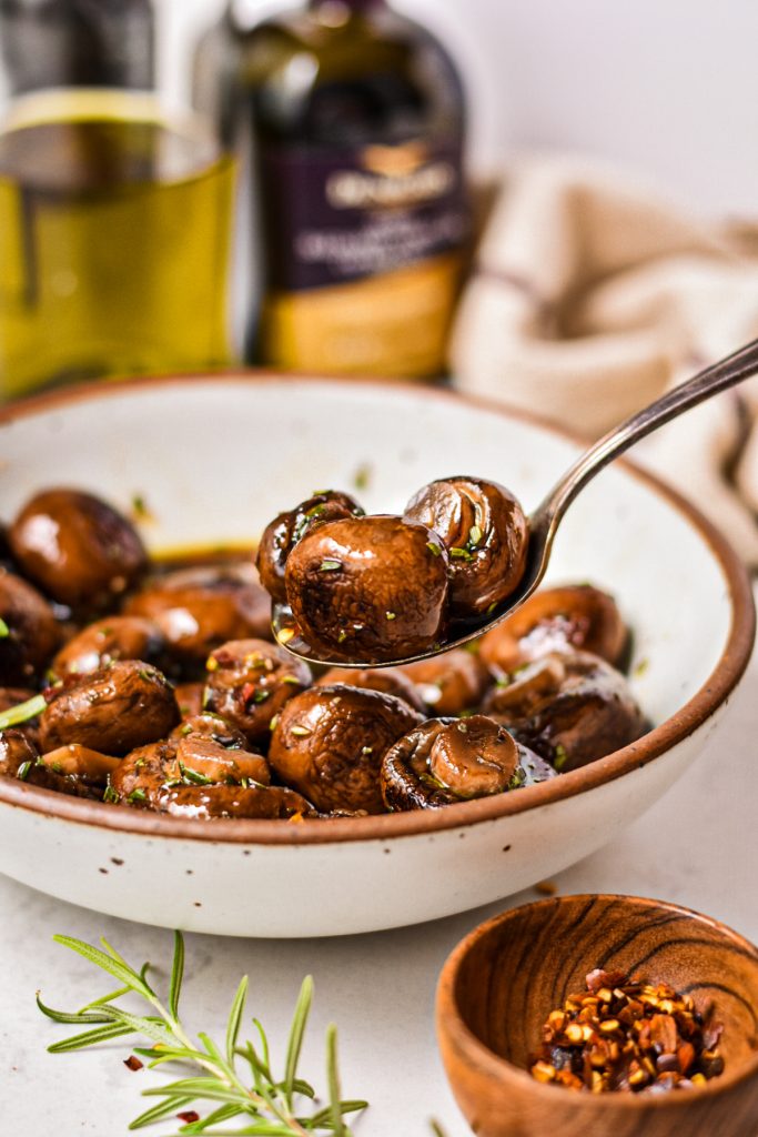 Spoon scooping up some balsamic marinated mushrooms from a bowl.