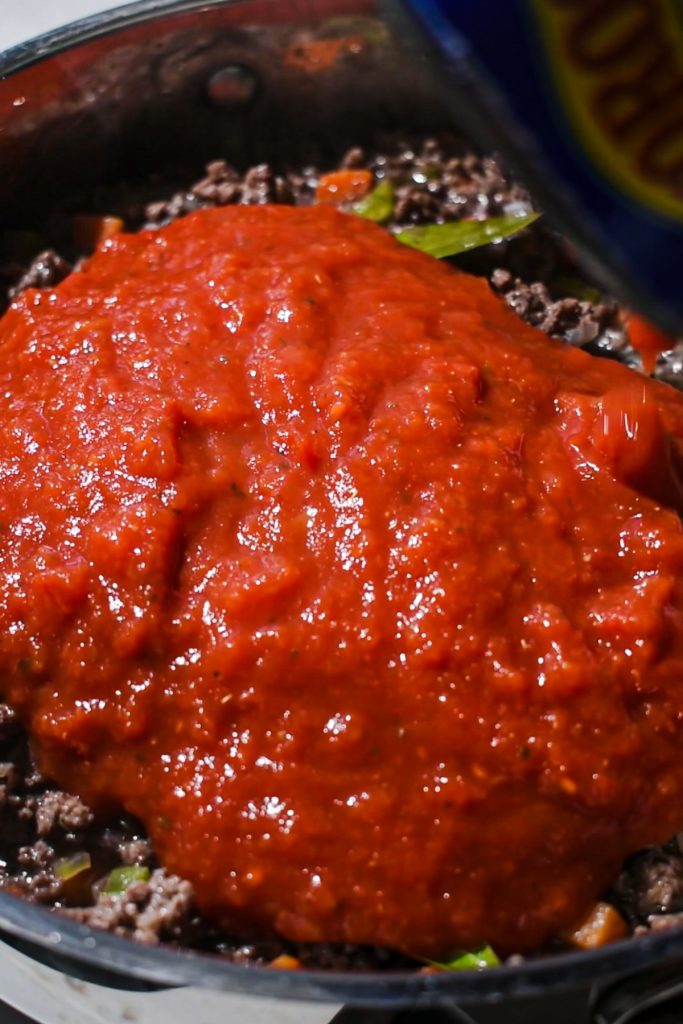 Crushed tomatoes added to the meat mixture in a skillet to make a meat sauce.