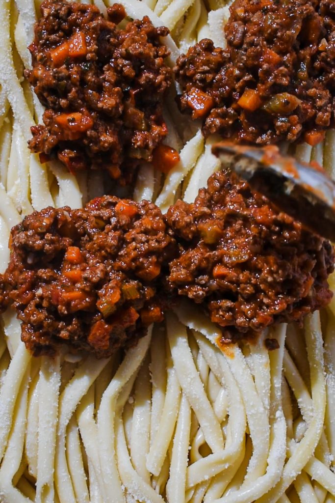 Cooked noodles being layered with the meat sauce on top.