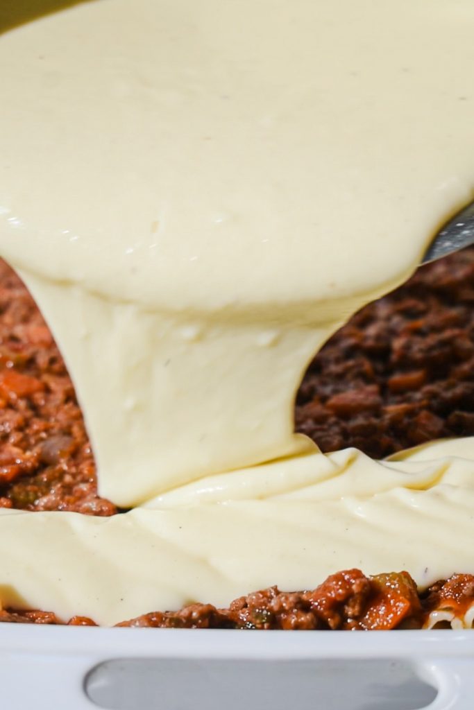 Bechamel sauce being layered on top of the meat sauce in a baking dish.