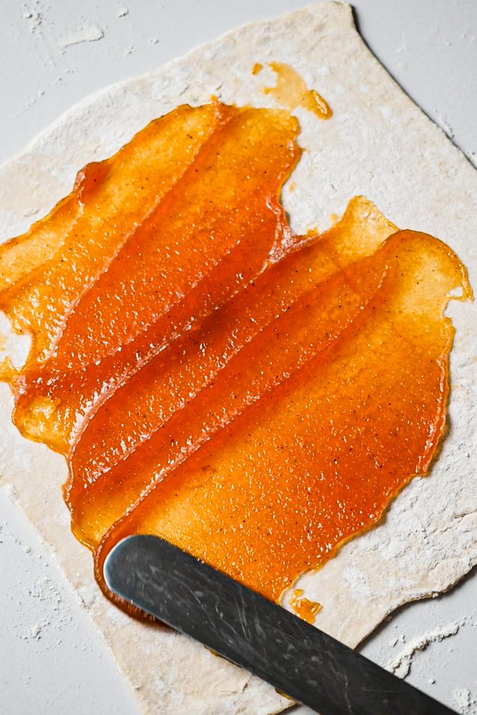 Spreading pumpkin butter on a sheet of puff pastry with an offset spatula.