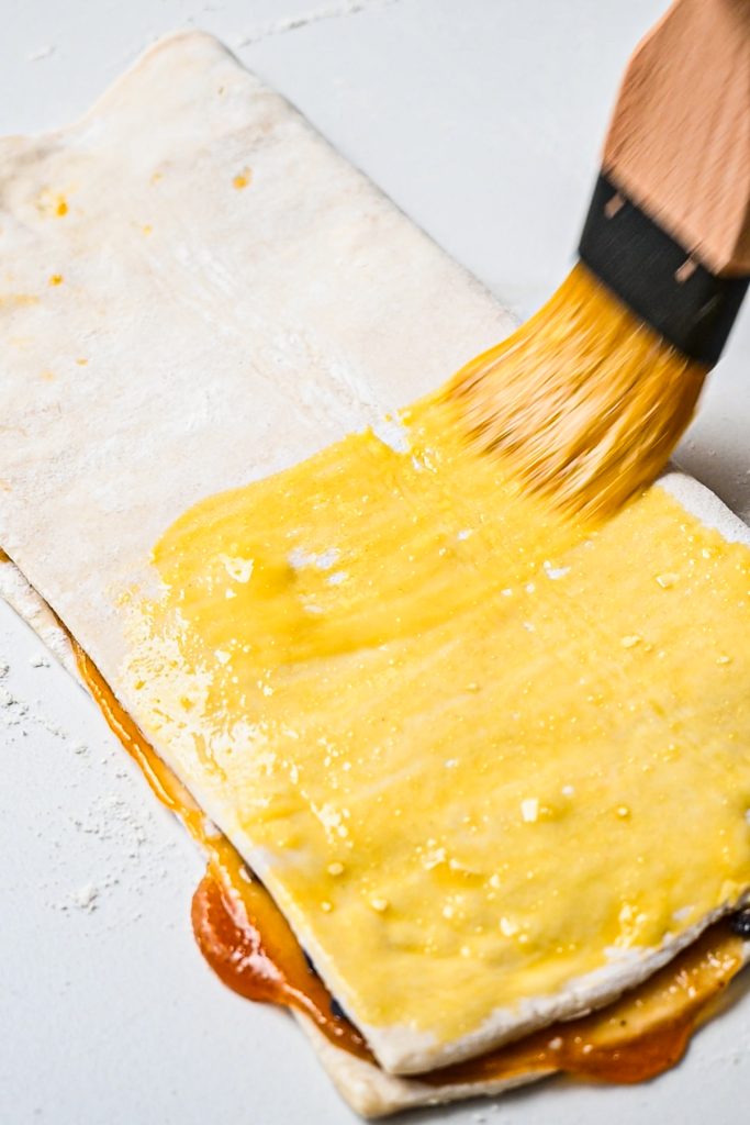 Brushing an egg wash on the outside of the puff pastry.