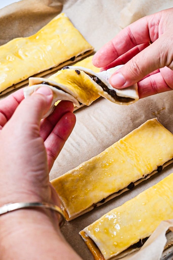 Using two hands to twist the rectangular puff pastry pieces.