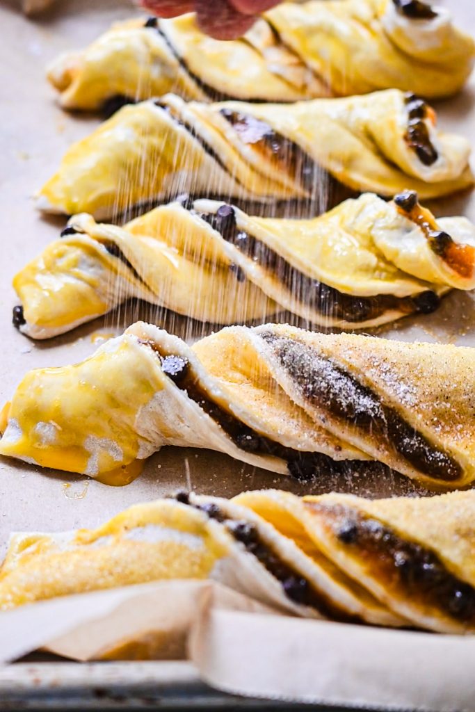 Sprinkling powdered sugar on top of the pumpkin butter and chocolate chip twists before baking.