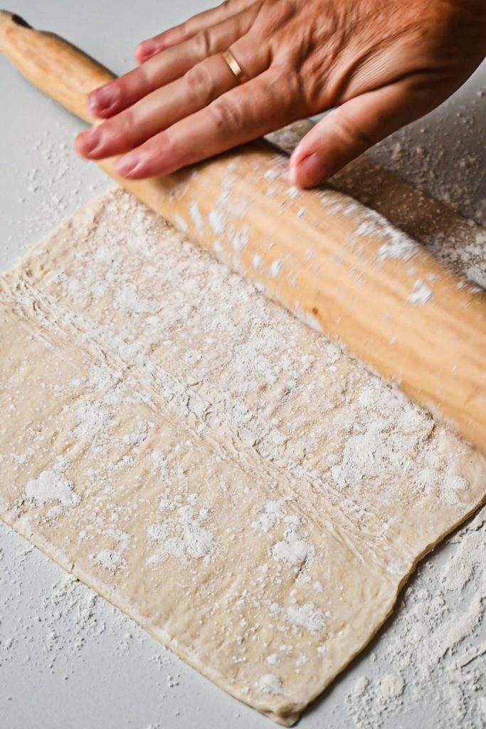 Using a rolling pin to flatten out a sheet of puff pastry.